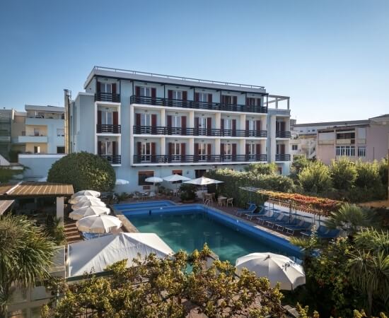 Hotel blu con piscina, ombrelloni e alberi verdi circostanti.