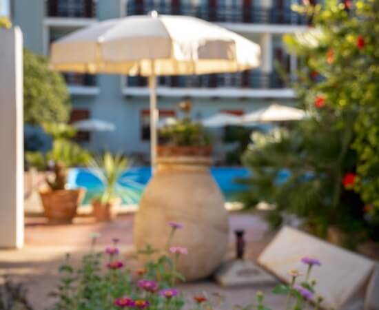 Area esterna con piscina, piante in vaso e ombrello bianco.