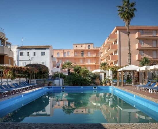 Piscina blu con lettini, gazebi e palme sullo sfondo.