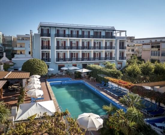 Piscina all'aperto con ombrelloni e lettini, edificio sullo sfondo.