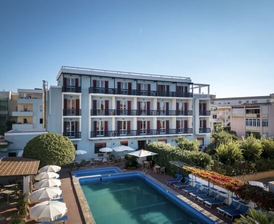 Hotel con facciata blu, piscina, ombrelloni e aree verdi.