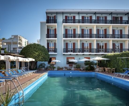 Edificio con balconi, piscina, lettini e ombrelloni sul deck.