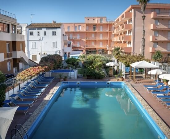 Piscina all'aperto con lettini, ombrelloni e alberi circostanti.