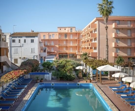 Piscina con lettini blu e edifici a più piani sullo sfondo.