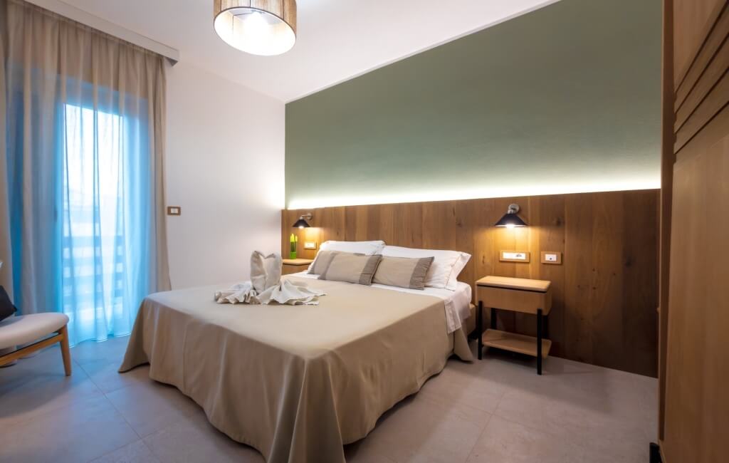 Camera d'hotel con letto beige, cuscini e asciugamani a forma di cigno.