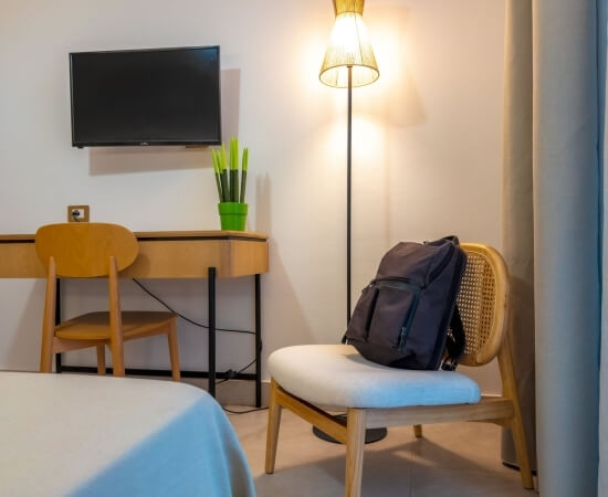 Zaino grigio scuro su sedia, lampada dorata e scrivania in legno.