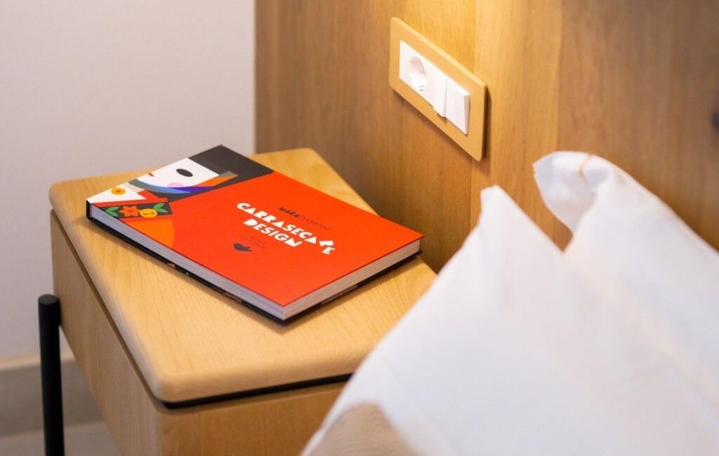 Libro "CARRASCA DESIGN" su un comodino accanto a un cuscino.