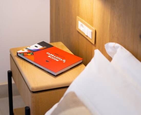 Un libro rosso su un comodino di legno accanto a un cuscino bianco.