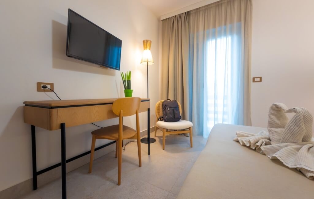 Camera d'hotel con TV, scrivania, piante e letto decorato.