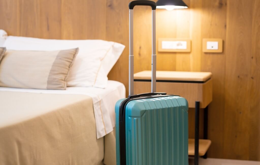 Valigia turchese accanto a un letto rifatto e parete di legno.