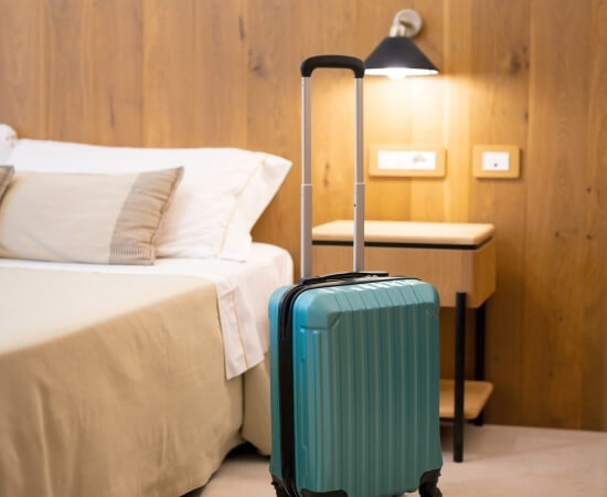 Valigia turchese accanto a un letto con coperta beige.