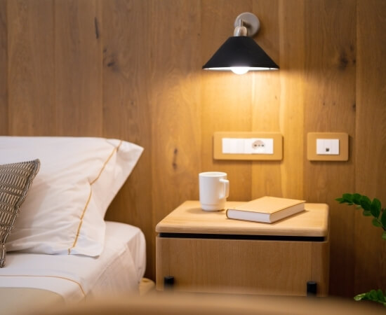 Area del letto con biancheria bianca, comodino e lampada nera.