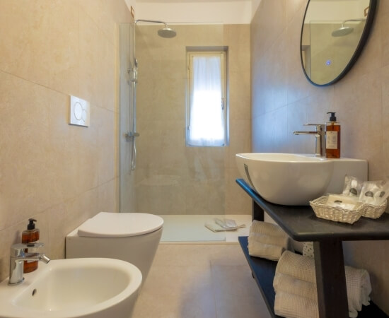 Bagno d'hotel con bidet, lavabo, doccia e scaffale di asciugamani.