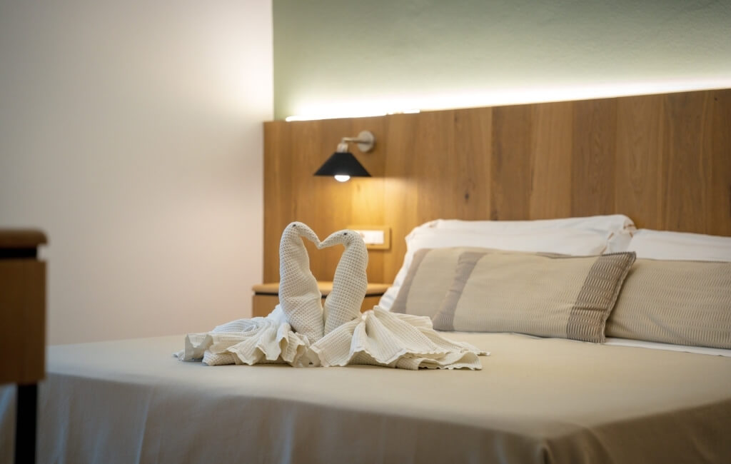 Camera d'hotel con letto, coperte beige e cigni di asciugamani.