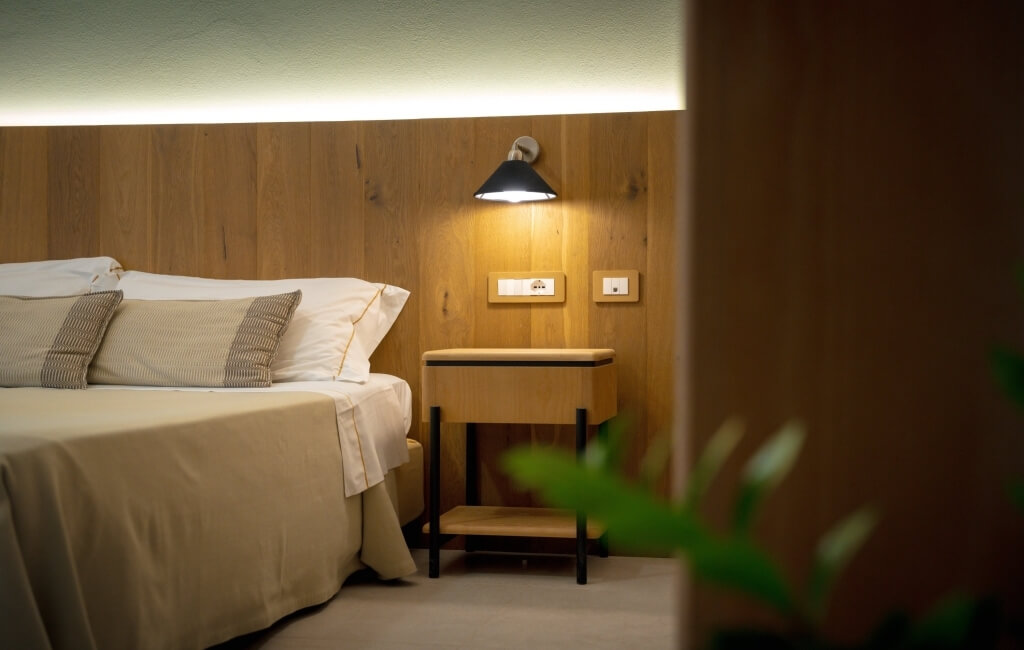 Camera d'hotel con letto, testiera in legno e lampada a muro.
