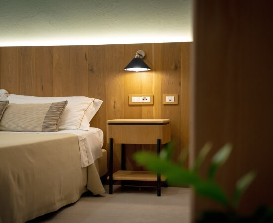 Camera d'hotel con letto bianco, tavolino e applique nera.