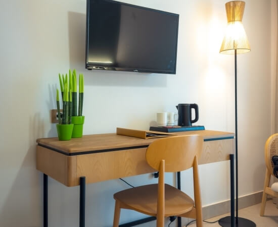 Hotel room desk with plants, mugs, kettle, and books.