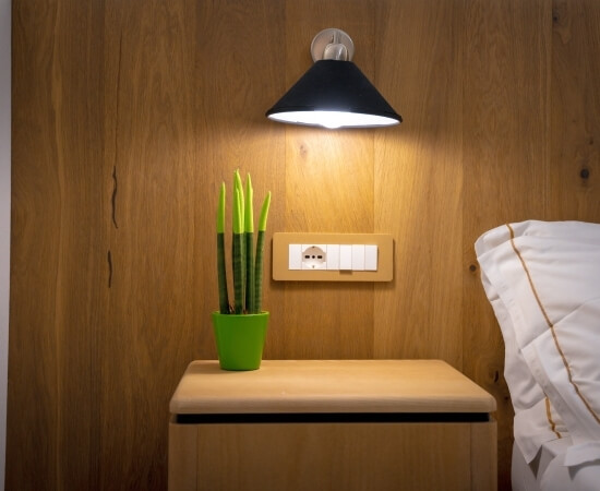 Tavolino in legno con pianta, applique nera e letto bianco.