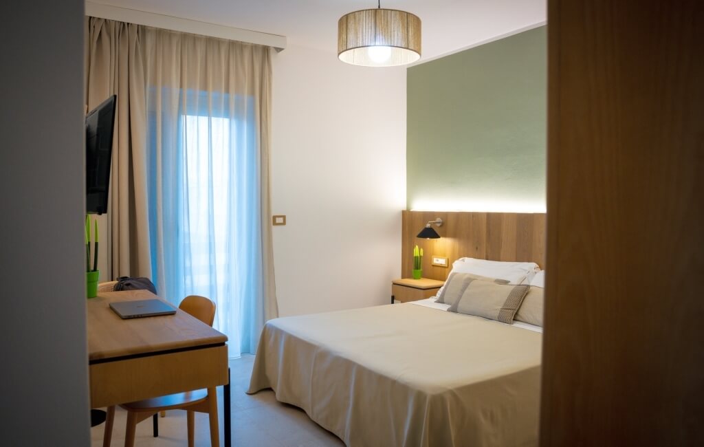 Camera d'hotel con letto, scrivania, TV e finestra.