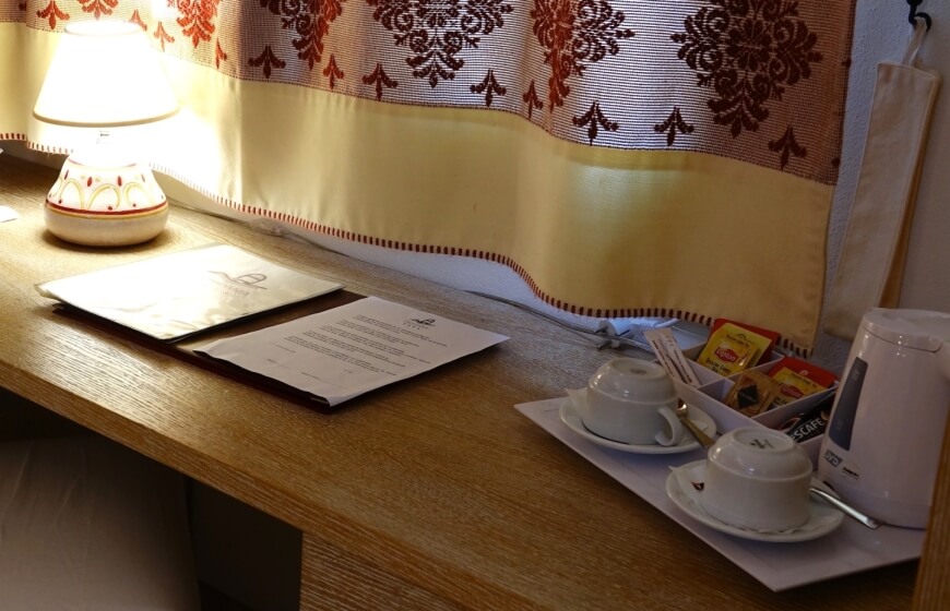 Wooden desk with lamp, documents, teacups, kettle, and utensils.