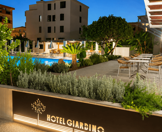 Area esterna dell'hotel con piscina, sedie e insegna illuminata.