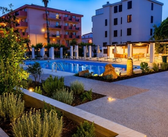 Area piscina con lettini, ombrelloni e piante decorative.