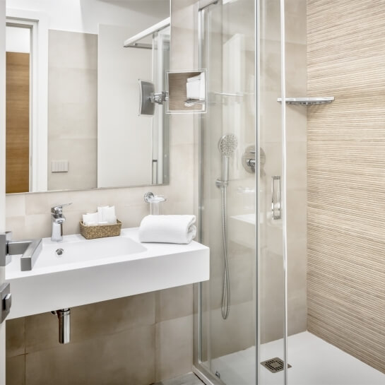 Bagno moderno con lavabo bianco, doccia in vetro, specchio con cornice argentata e pannelli in legno chiaro.