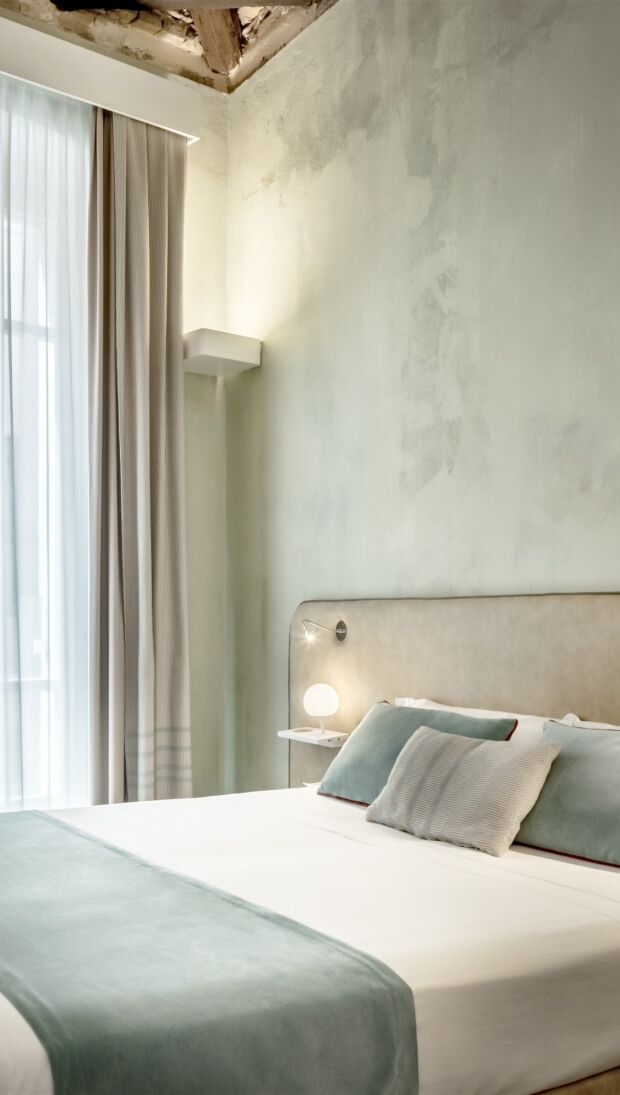Camera da letto con letto elegante, lampada calda, finestre con tende grigie e pareti verde chiaro.
