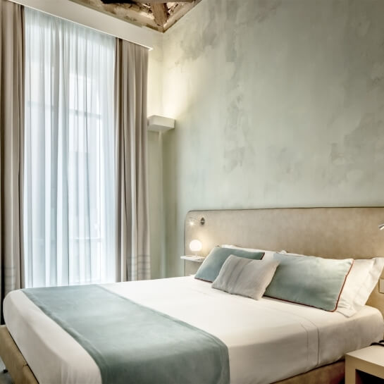 Camera serena con letto grande, biancheria bianca e grigia, luce naturale e decorazioni che invitano al relax.