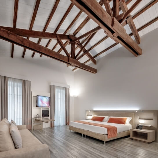 Camera con letto matrimoniale, divano beige, pareti bianche e dettagli in legno chiaro, atmosfera tranquilla.