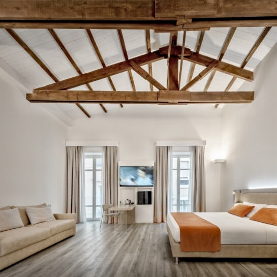 Modern hotel room with a large bed, cream couch, and bright windows, featuring minimalist decor and a serene atmosphere.