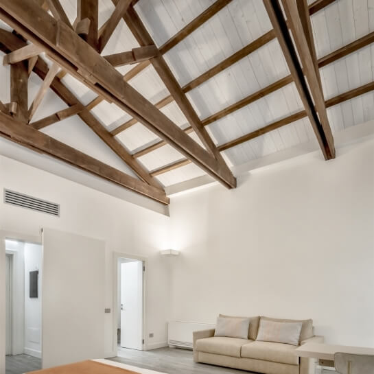 Minimalist room with white walls, wooden ceiling, cream couch, small table, and doorway, creating a bright and inviting atmosphere.