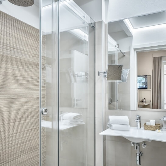 Modern bathroom with glass shower, white sink, large mirror, and minimalist design; doorway to another room in background.
