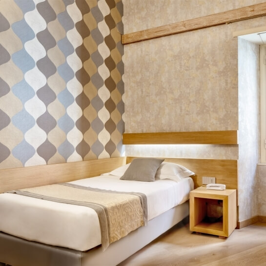 Camera da letto serena con letto bianco, pareti decorate e luce naturale che illumina il pavimento in legno chiaro.