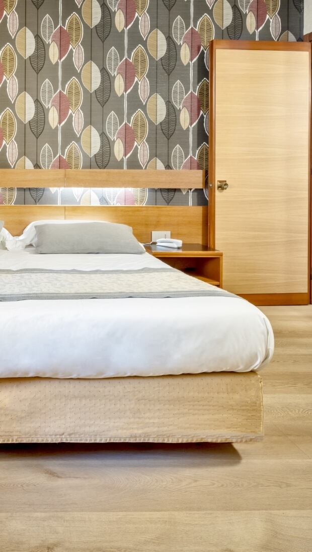 Camera da letto con letto bianco, comodino, armadio e carta da parati a motivi fogliari. Atmosfera rilassante.