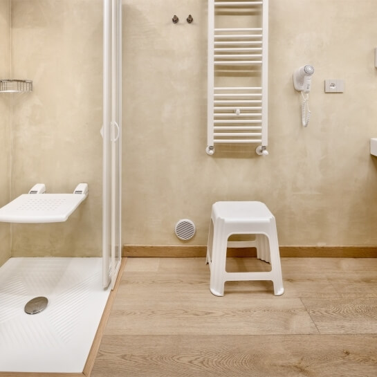 Area doccia elegante con toni beige, porta in vetro, sedile ribaltabile e dettagli funzionali in un'atmosfera serena.