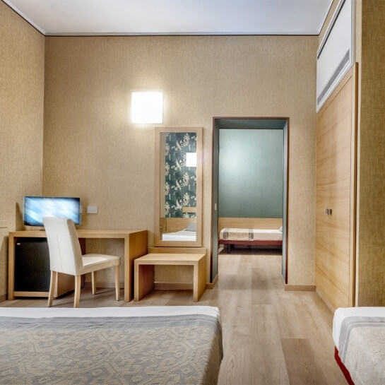 Camera d'hotel con due letti, scrivania, sedia, pavimento in legno chiaro e pareti beige.