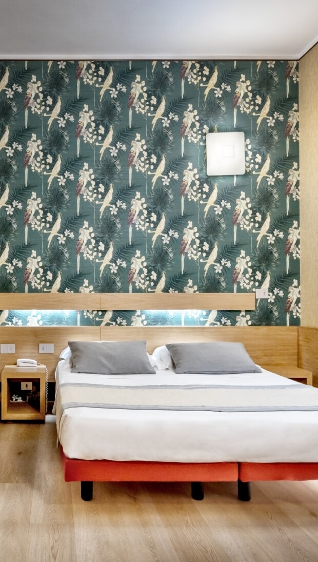 Camera da letto con letto centrale, comodino, carta da parati tropicale teal e pavimento in legno chiaro.
