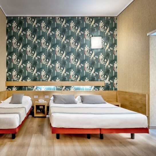 Camera d'hotel con due letti, parete verde e bianca, pavimento in legno chiaro e atmosfera minimalista.
