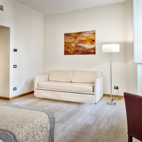 Una stanza minimalista e accogliente con un divano bianco, lampada, pittura astratta e un letto grigio e bianco.