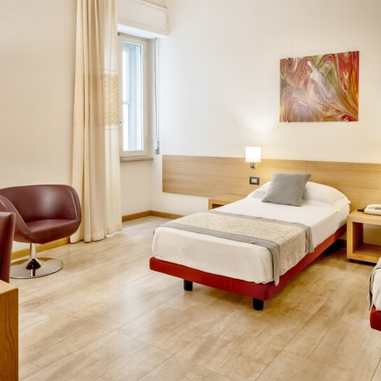 Camera d'hotel serena con letto bianco, arredamento elegante, pareti chiare e una finestra con tende bianche.