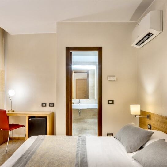 Camera da letto con scrivania minimalista, sedia rossa, armadio, letto con cuscini grigi e condizionatore d'aria.