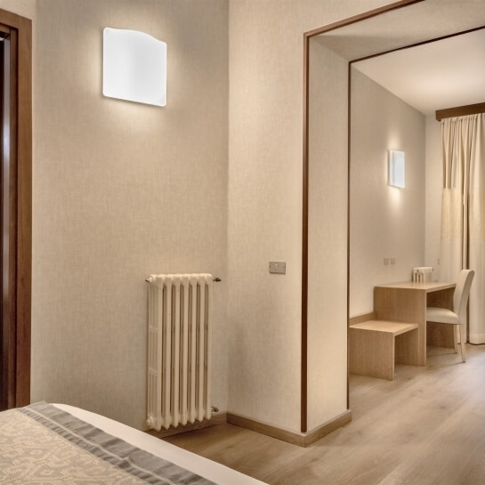 Camera d'hotel moderna con radiatore, sconce, comò, finestra con tenda e letto visibile sullo sfondo.