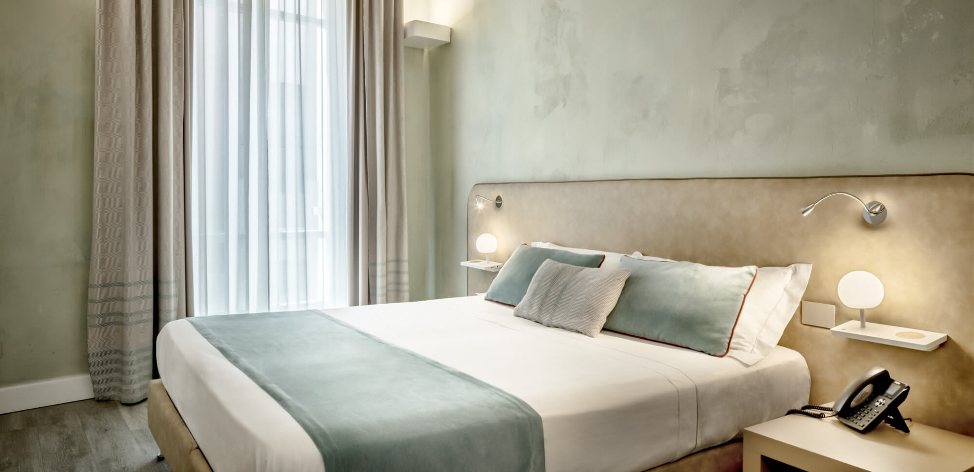 Camera d'hotel con letto, cuscini blu, pareti verdi e pavimento in laminato.