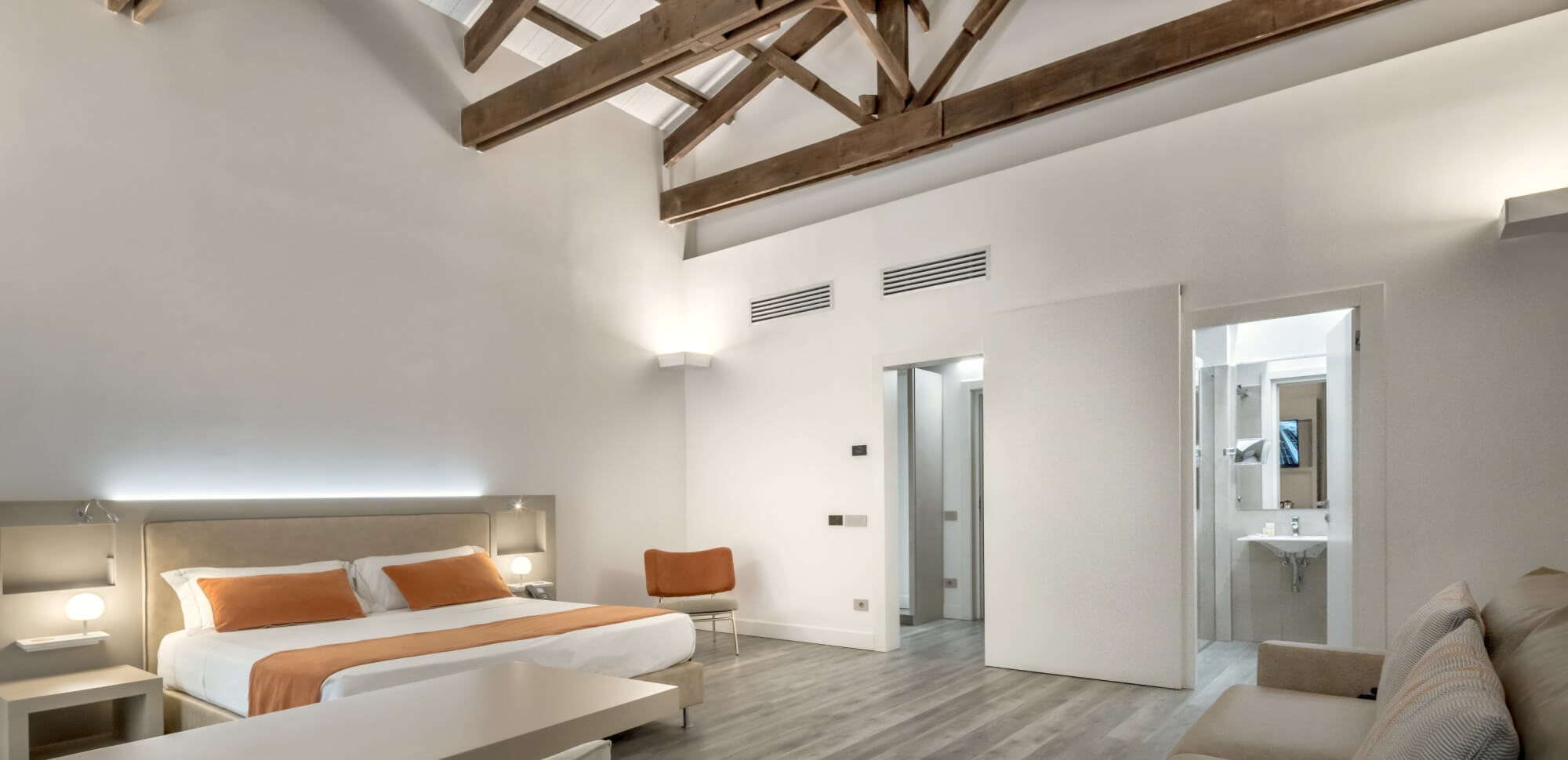 Camera d'hotel con letto king-size, decorazioni arancioni e bagno visibile.