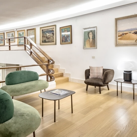 Seating area with green sofas, brown armchair, and staircase.
