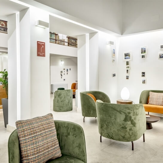 Lobby con poltrone verdi, divano arancione e tavolino con lampada.