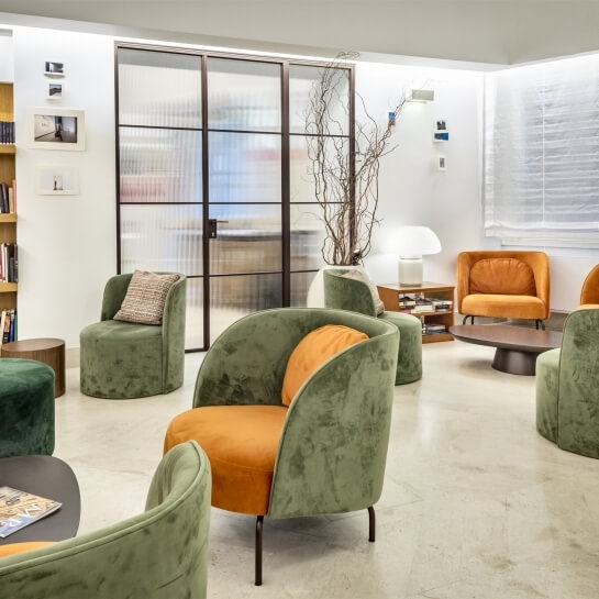Lounge area with colorful chairs, coffee table, bookshelf, and plant.