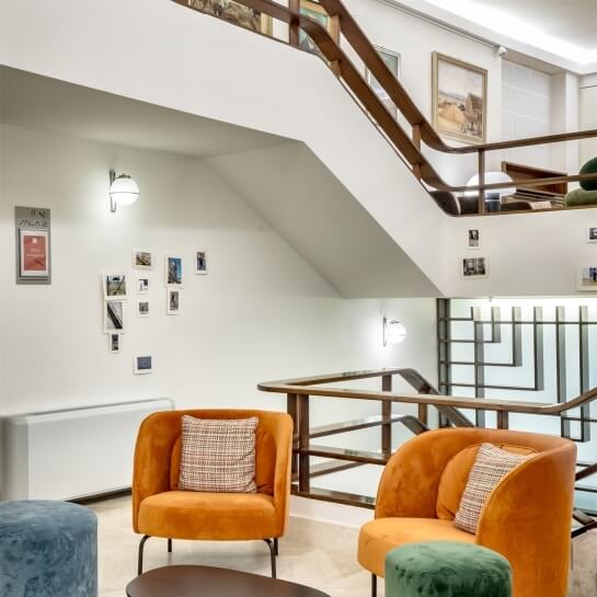 Indoor seating area with orange chairs, ottomans, and wooden staircase.
