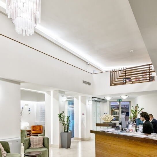 Hotel lobby with wooden reception desk, chandelier, chairs, and plants.